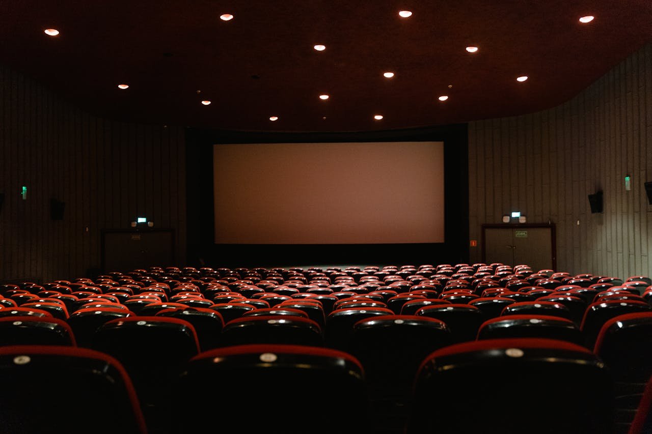 About A dimly lit empty cinema theater with rows of red chairs facing a projector screen.