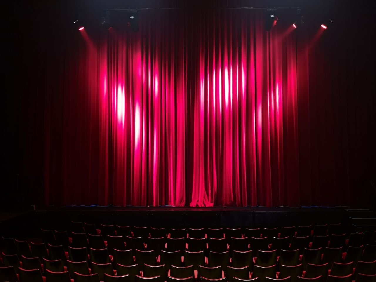 Home Empty theater stage with red curtains and seating, ready for a performance.